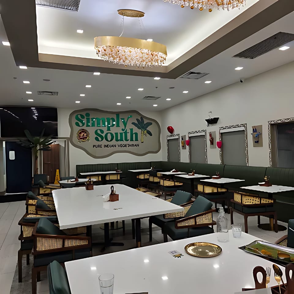 Interior of Simply South restaurant with white tables, dark green chairs, and a large logo on the wall.