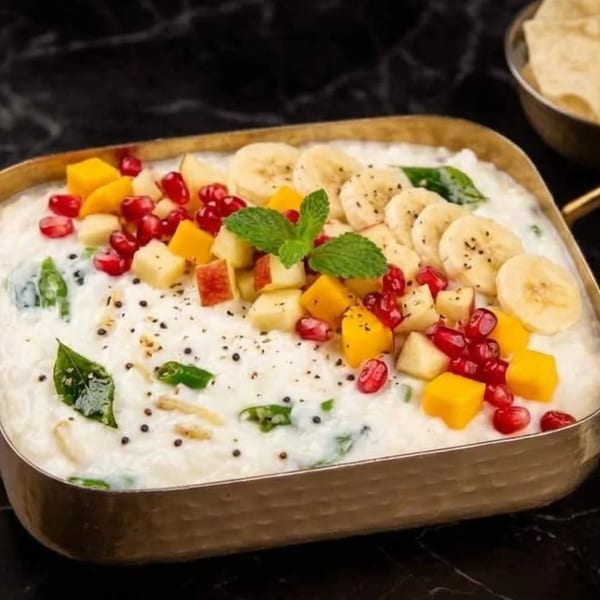 Creamy yogurt dish topped with colorful diced fruits, pomegranate seeds, and mint in a brass bowl.