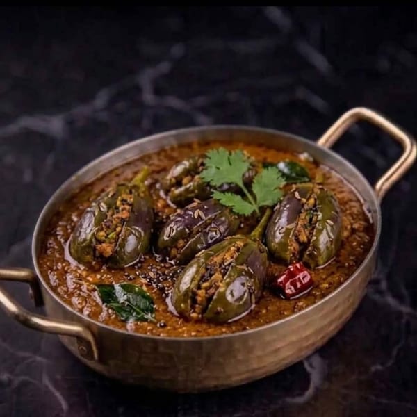 Stuffed baby eggplants in a rich, dark gravy, garnished with fresh cilantro in a brass pot.