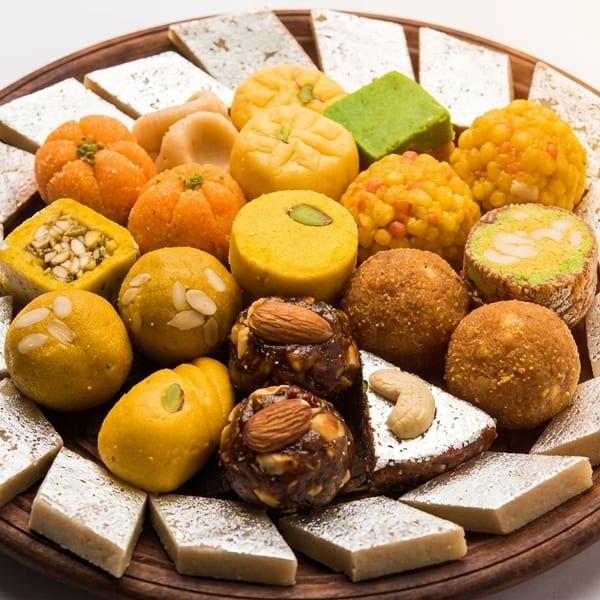 Assorted colorful Indian sweets like kaju katli and ladoos arranged on a wooden platter.